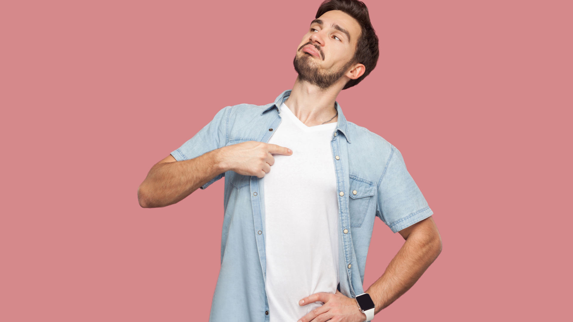 Brunette man in white t-shirt and jean over-shirt pointing at his chest and looking proud. Pink background.