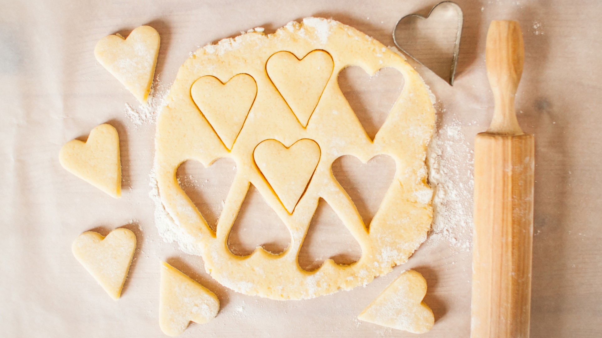 Yellow batter having been cut into shapes of love hearts with a rolling pin right next to it. Some flour on batter.