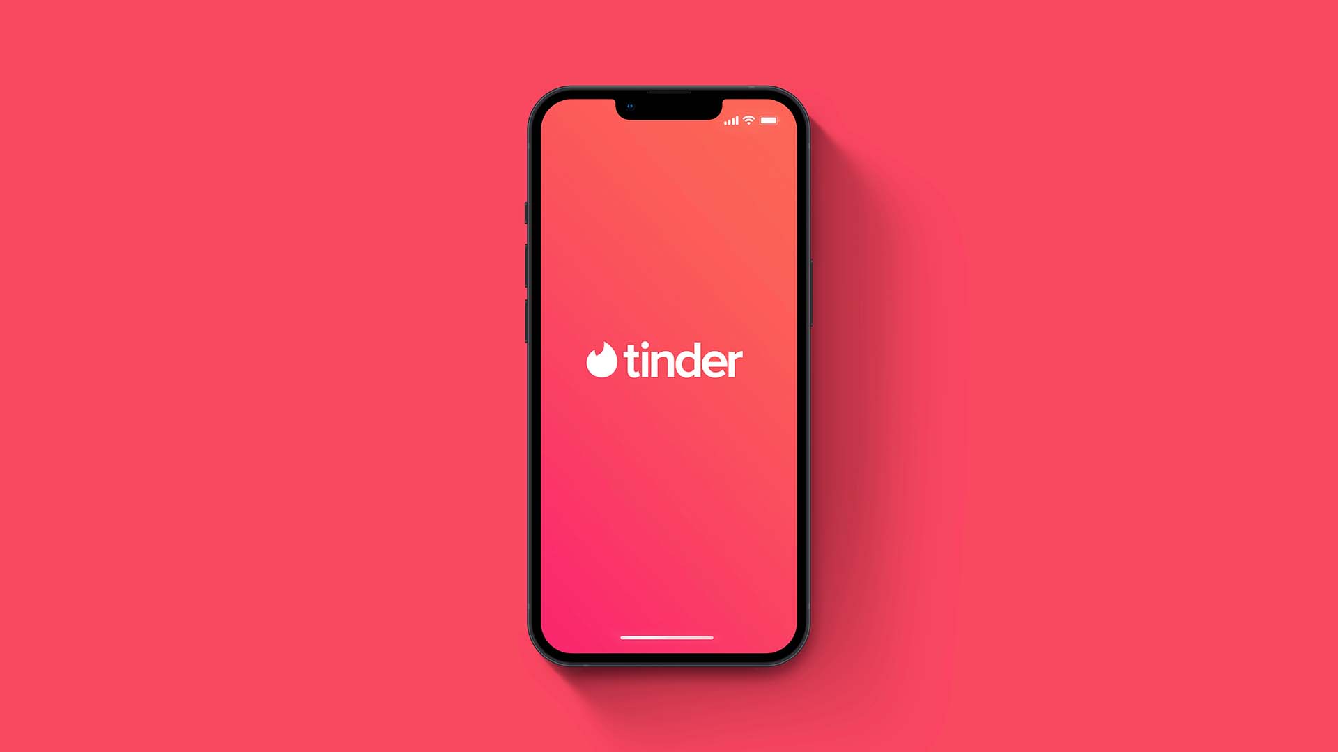 Mobile phone in front of coral background. The phone's screen has the same color with a white tinder logo at the center.