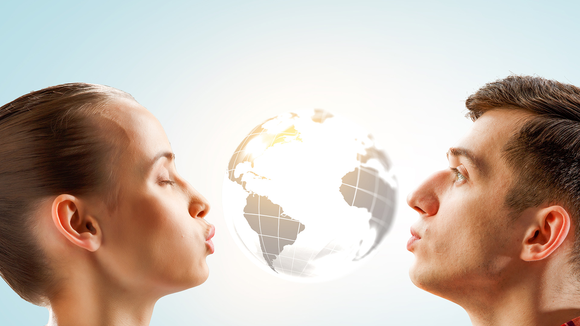 Brunette man and woman facing each other and leaning in for a kiss, with a white globe between them.