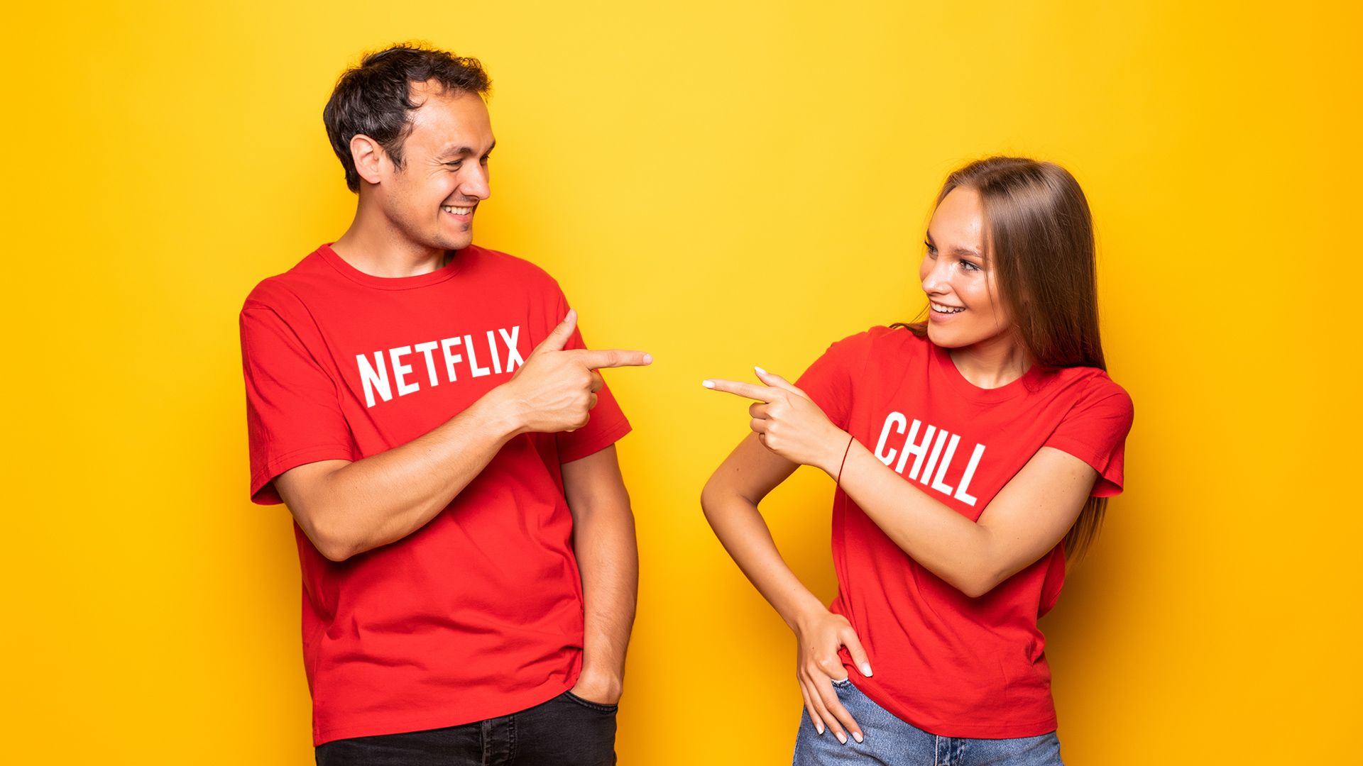 Woman and man red shirt pointing finger guns at each other. The man's shirt reads 'Netflix' and the woman's reads 'Chill'.