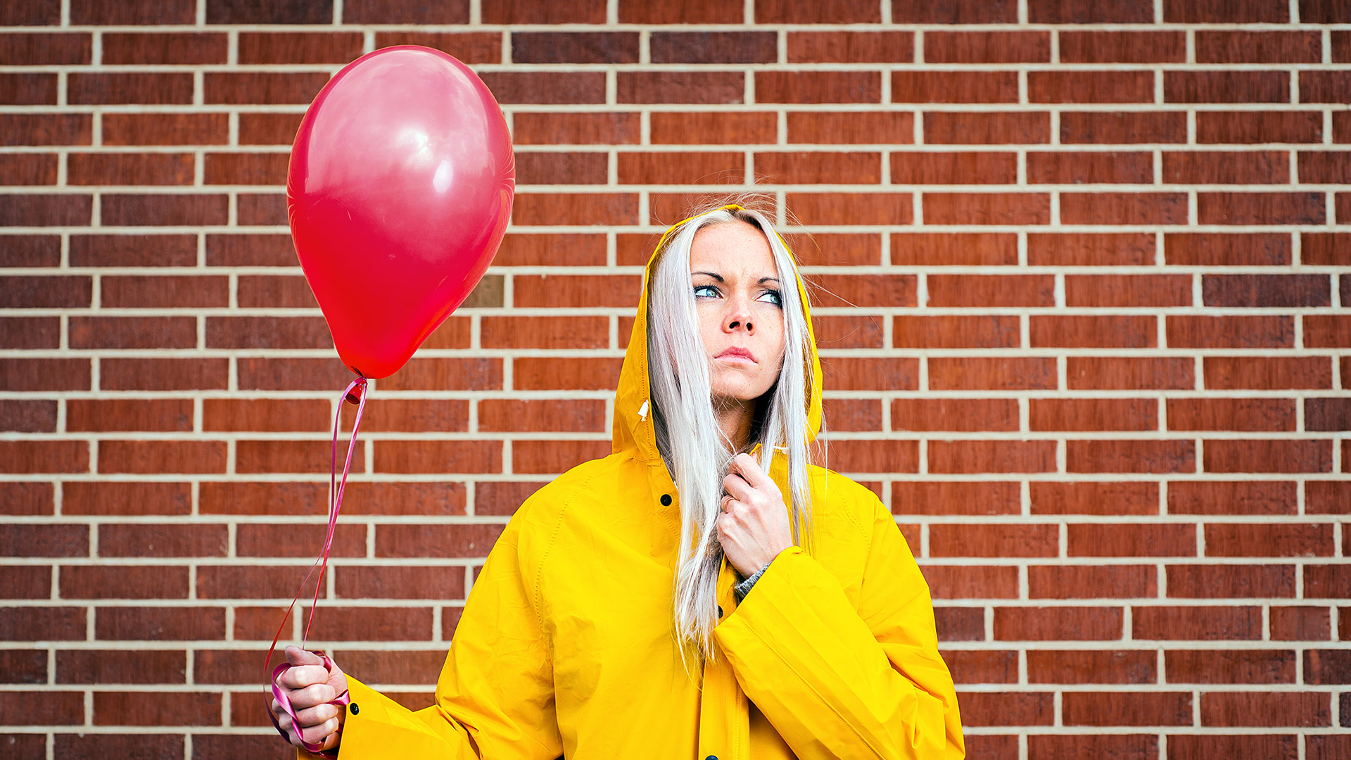 Woman holding a red balloon while wearing a bright yellow raincoat.