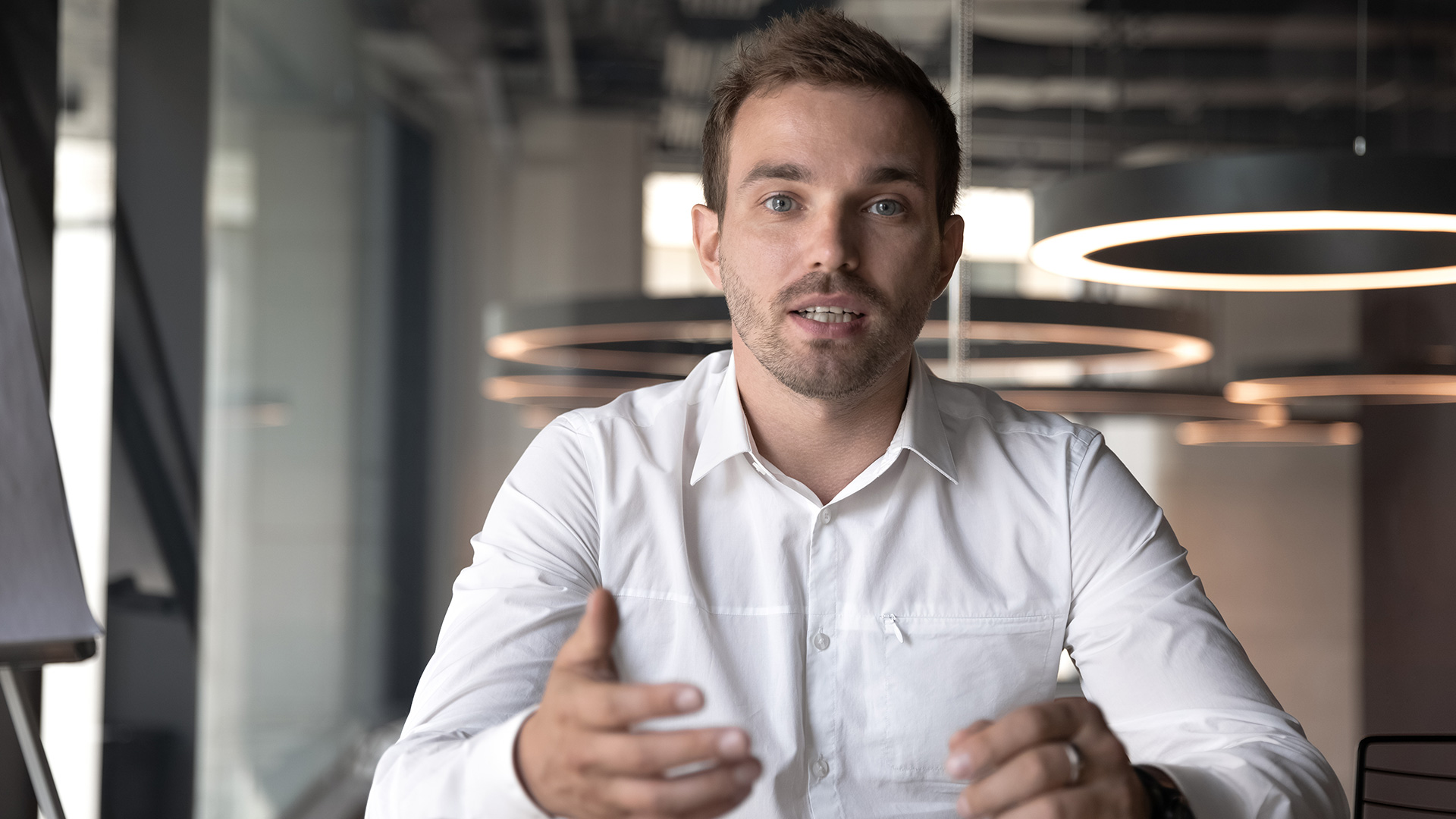 Young man with blue eyes and white button-up having a serious conversation while moving his hands in front of him.