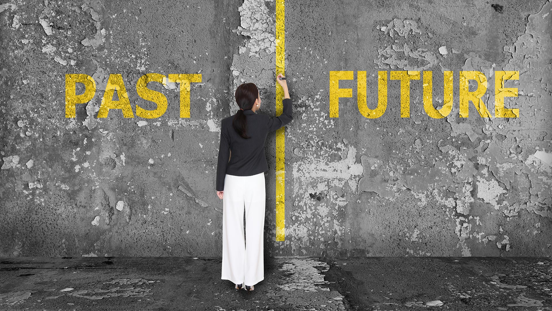 Brunette woman drawing a yellow line between the words 'PAST' and 'FUTURE' which are written on a grey wall.