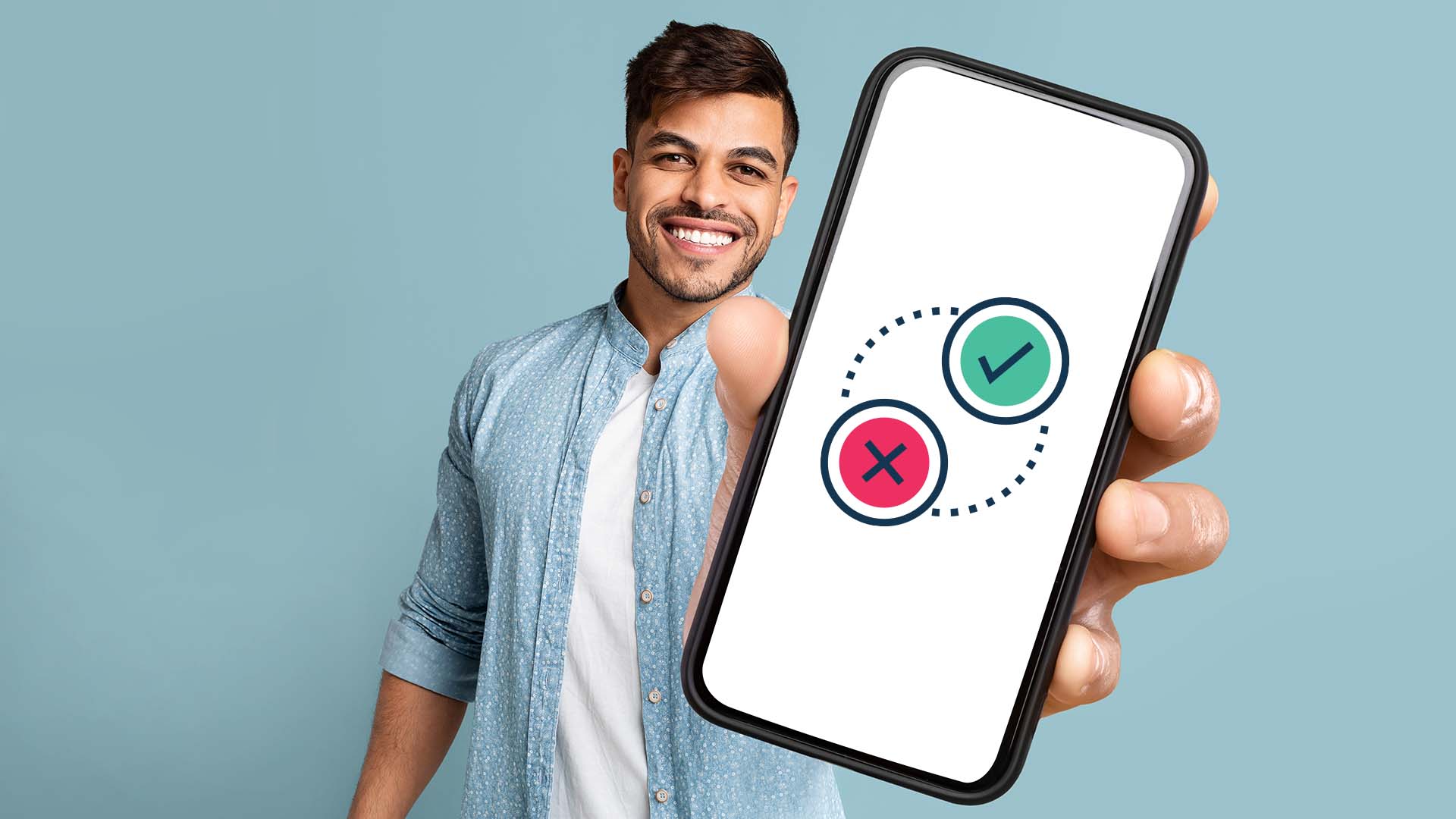 Brunette man in light blue shirt standing in front of green wall, showing his phone screen featuring a 'tick' and 'x' button.