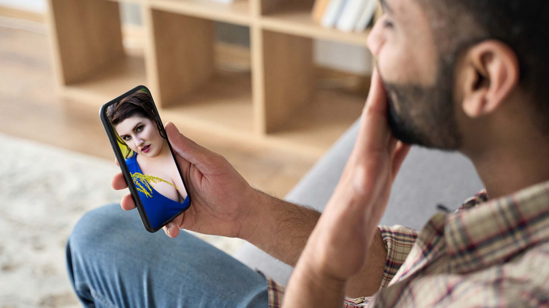 Man holding his palm against his lips while holding his phone with his other hand. The screen shows a brunette BBW.