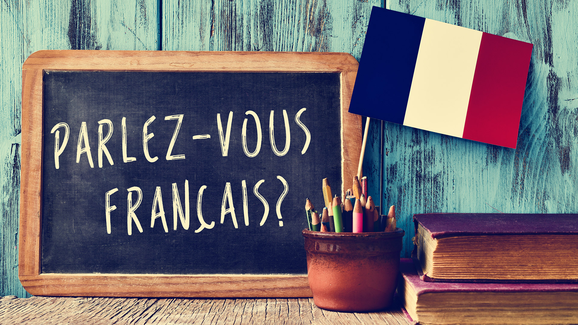 Chalk board reading Parlez-vous francais? with a cup full of pencils and the flag of France right next to it.