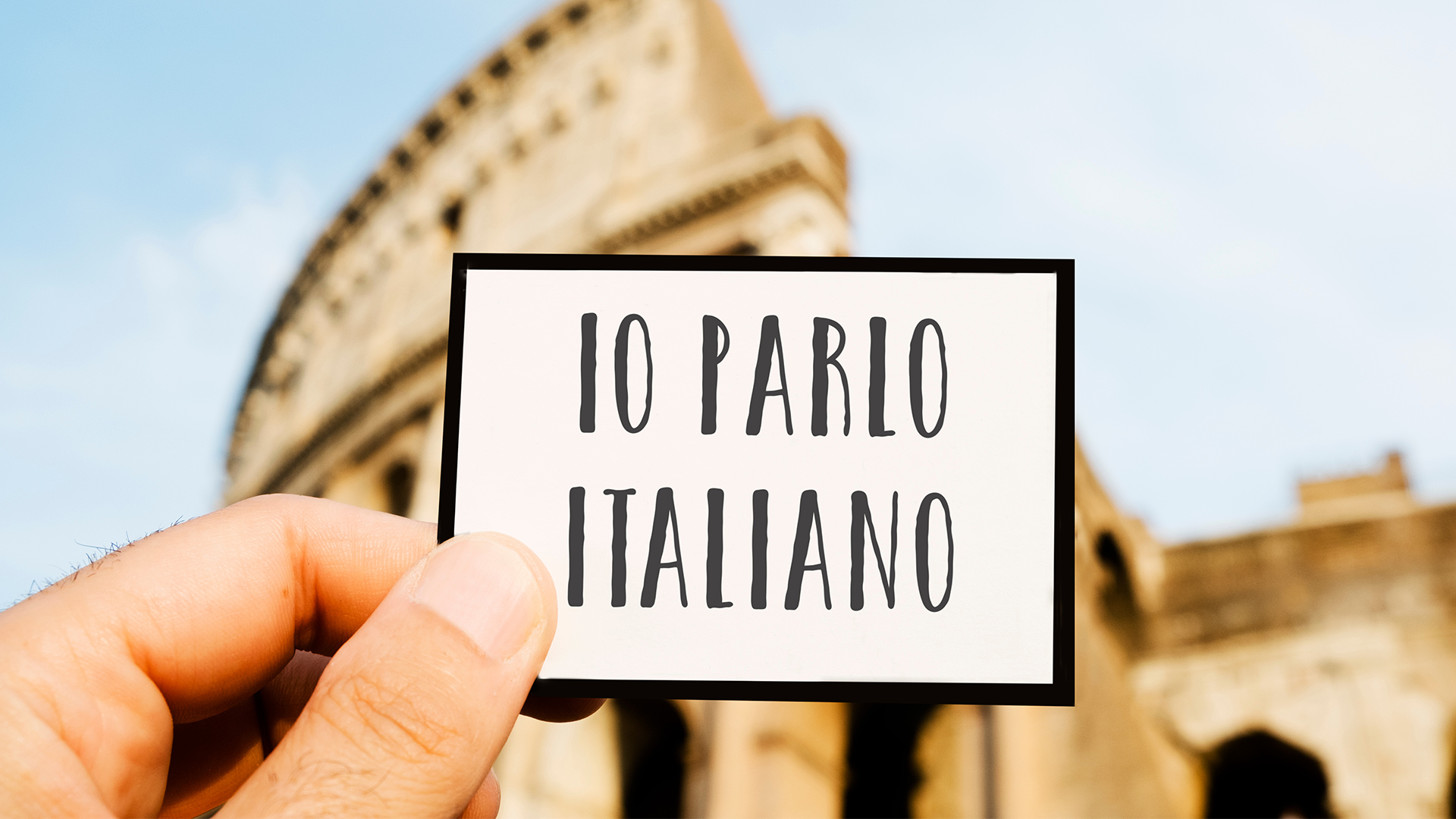 Card reading IO PARLO ITALIANO being held up in front of the Rome Colosseum in Italy.