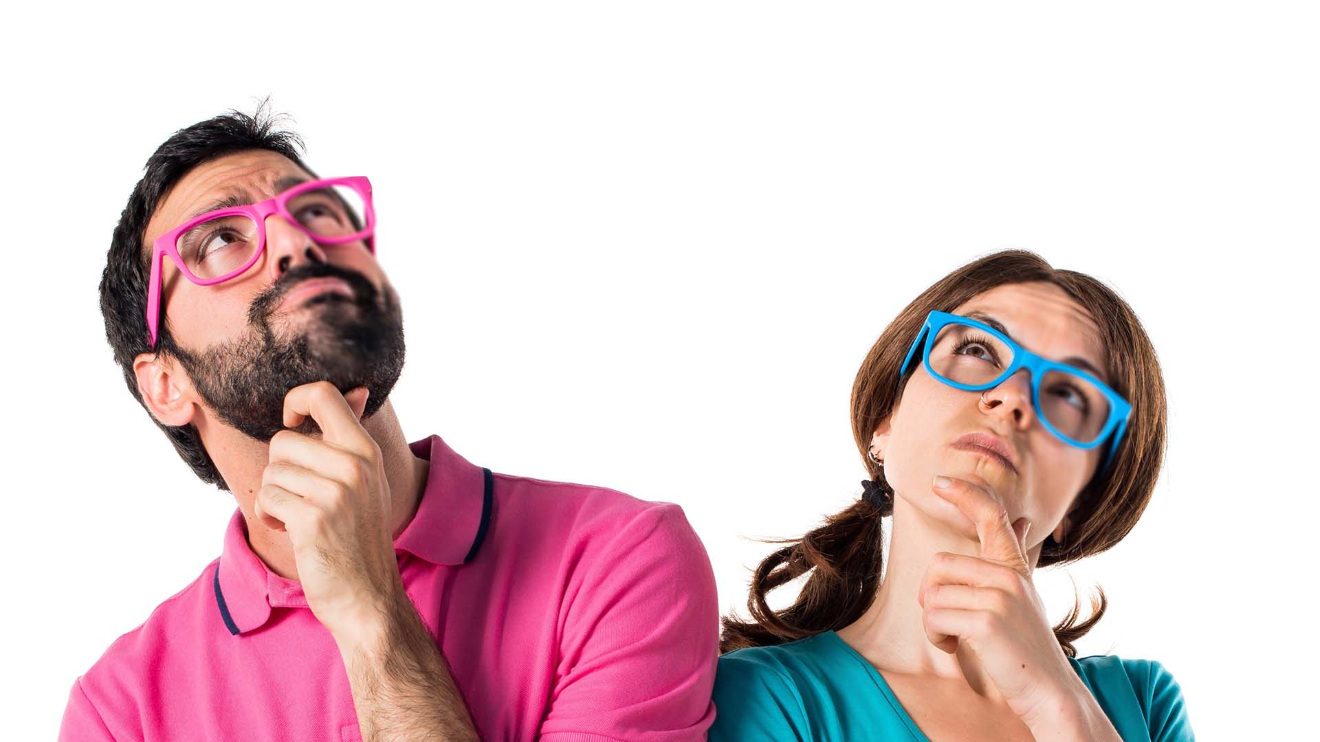 Brunette man in pink glasses and shirt and woman in blue glasses and shirt standing next to each other rubbing their chins.