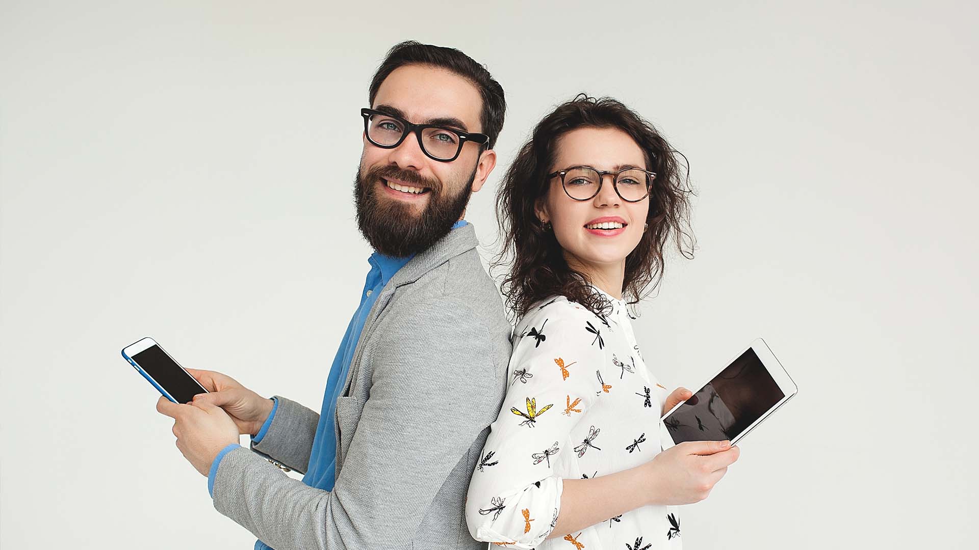 Brunette man and woman in glasses and professional clothing standing back to back to each other and holding tablets.