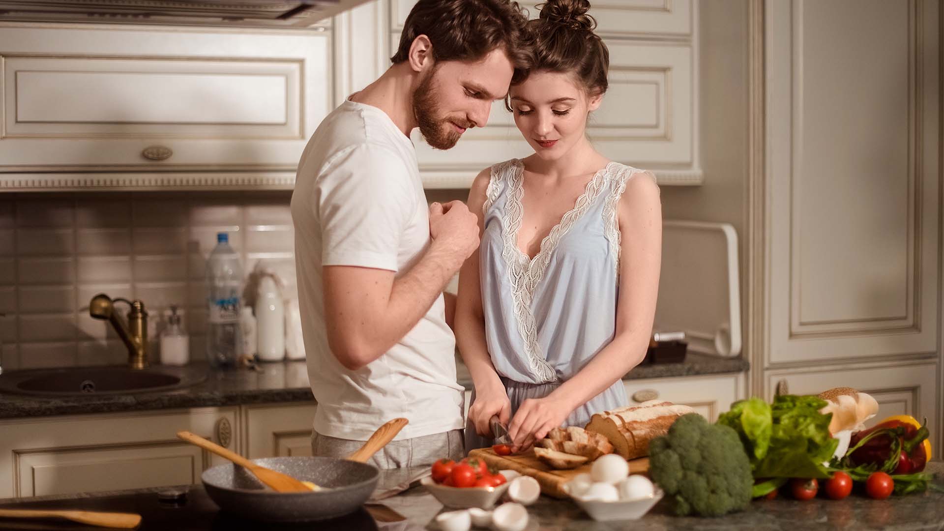Brunette man and woman standing next to each other in the kitchen in front of them a counter fool of different vegetables.
