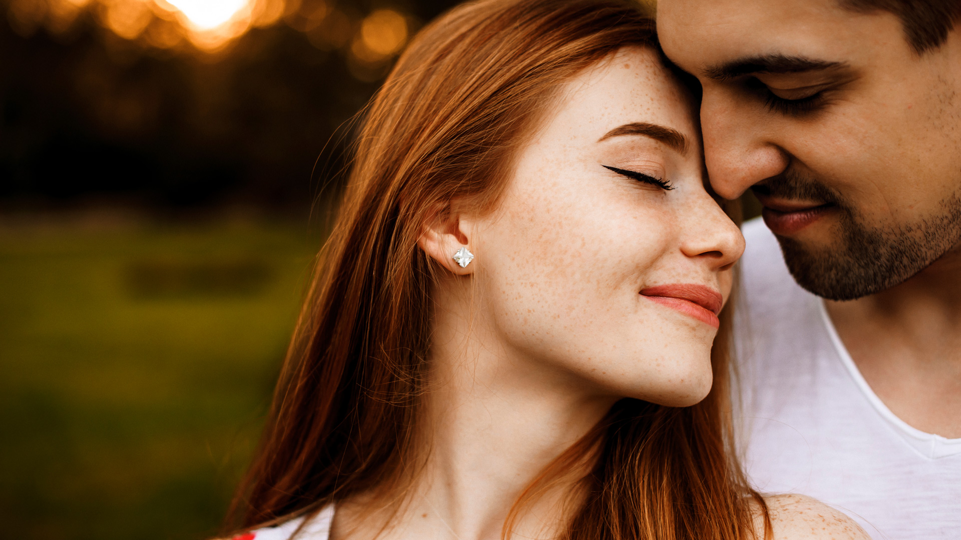 Red-haired woman and brunette man touching foreheads with each other with their eyes closed smiling.